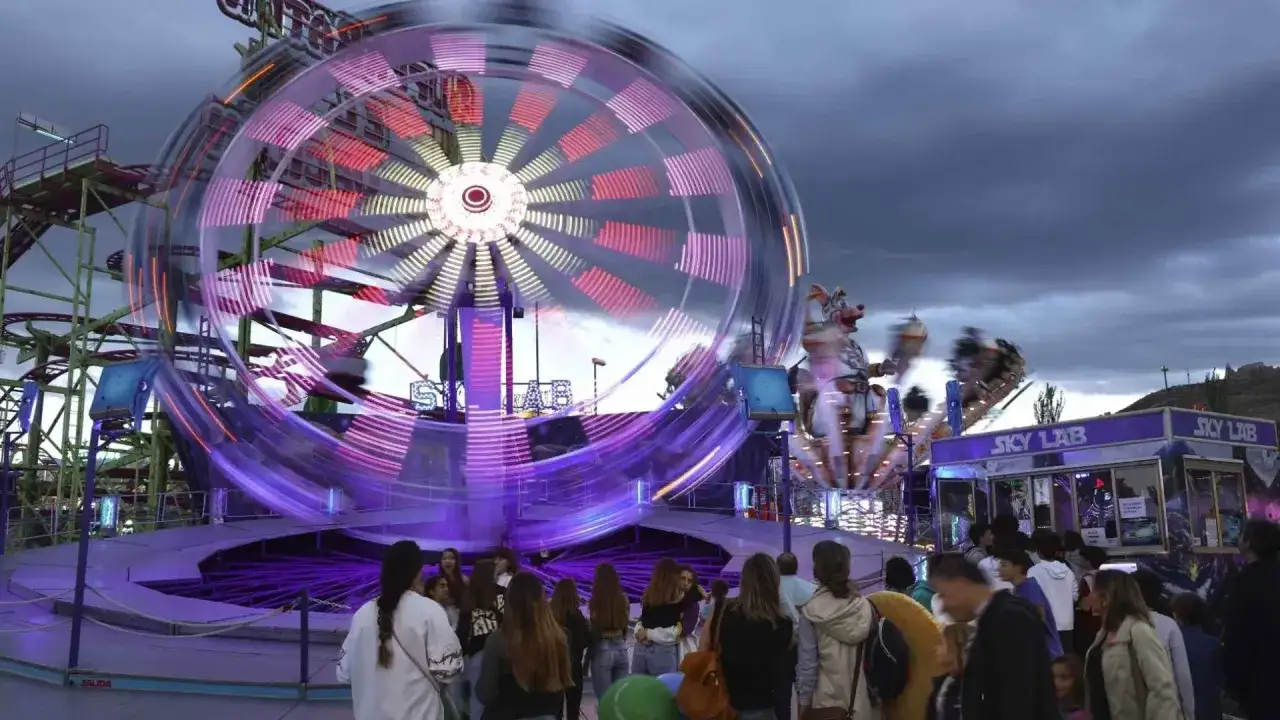 Atracciones giratorias iluminadas en el recinto ferial de Zaragoza. Gente esperando para subir.