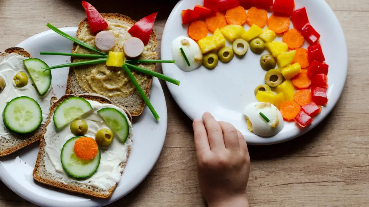 Kreative kinder rezepte: Brote mit Gurken, Oliven und Karotten als Gesichter, bunte Gem&uuml;sestreifen und Eier auf einem Teller.