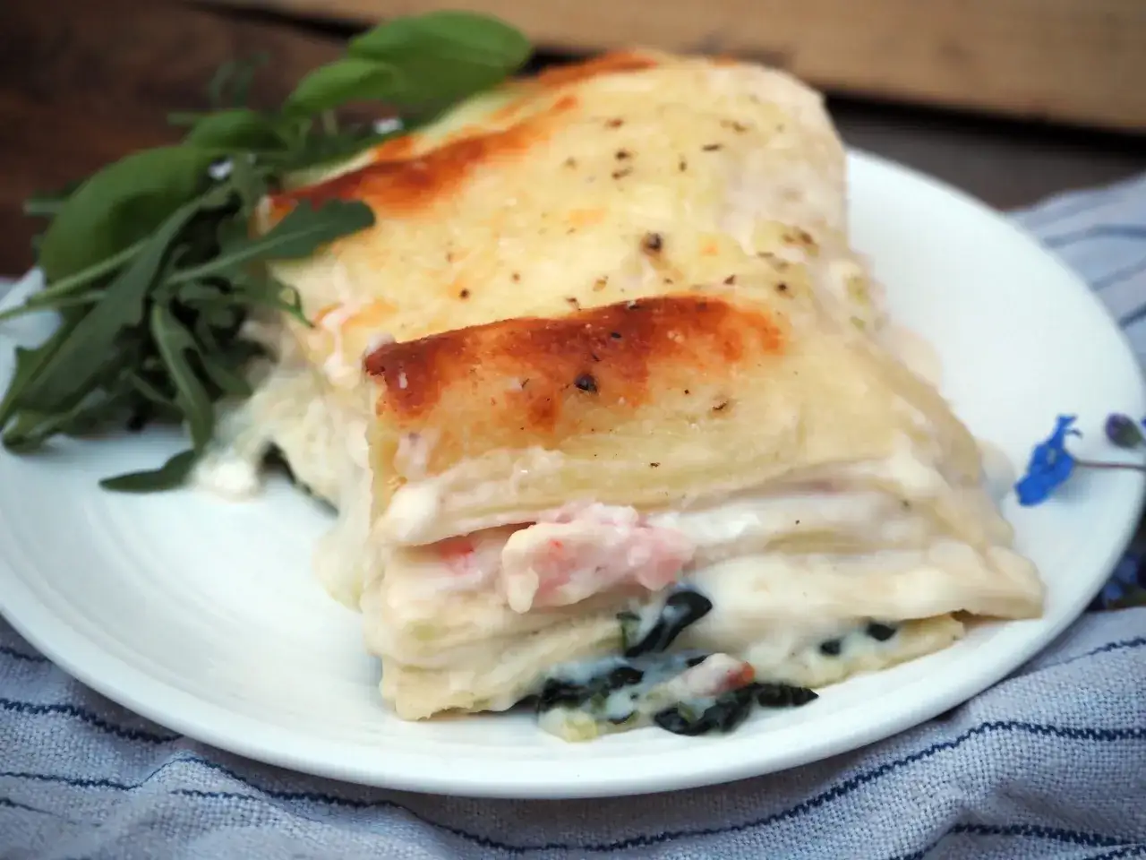 En krämig lasagne bianco med räkor och spenat, toppad med gyllene ost och garnerad med färska örter.