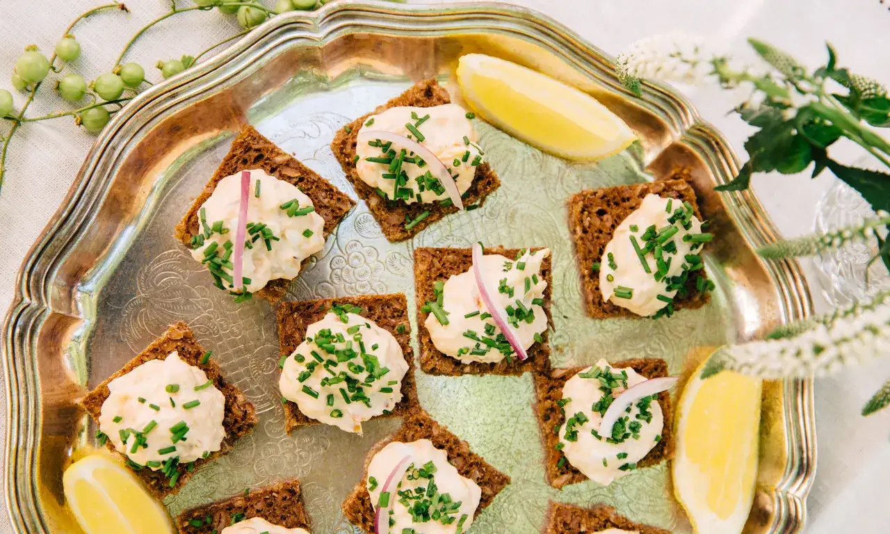 Snittar med lax och philadelphia p&aring; m&ouml;rkt br&ouml;d, toppade med gr&auml;sl&ouml;k och r&ouml;dl&ouml;k. Serveras p&aring; ett silverfat med citronklyftor.