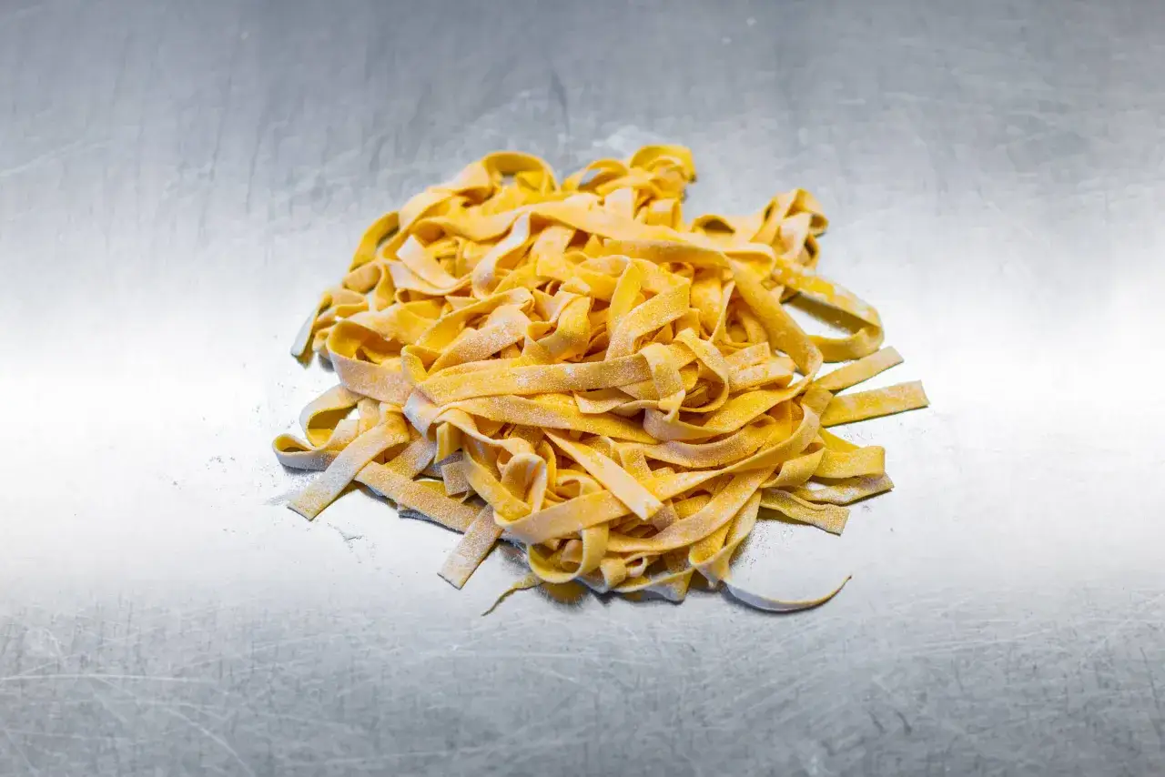 Frische, selbstgemachte Tagliatelle liegen auf einer metallischen Arbeitsfläche. Ein Beweis dafür, dass Tagliatelle selber machen gar nicht so schwer ist.