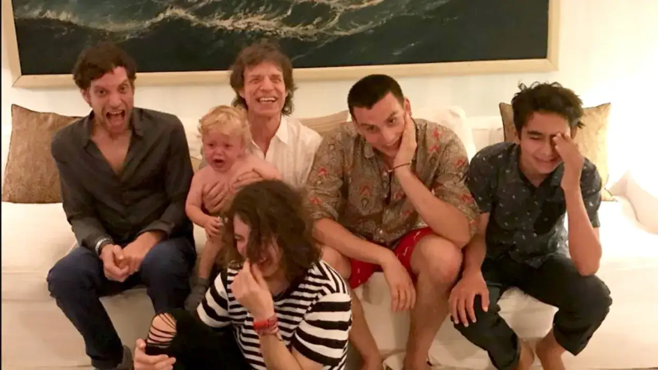 Mick Jagger z dziećmi na kanapie. Jedno z dzieci płacze, reszta się śmieje.
