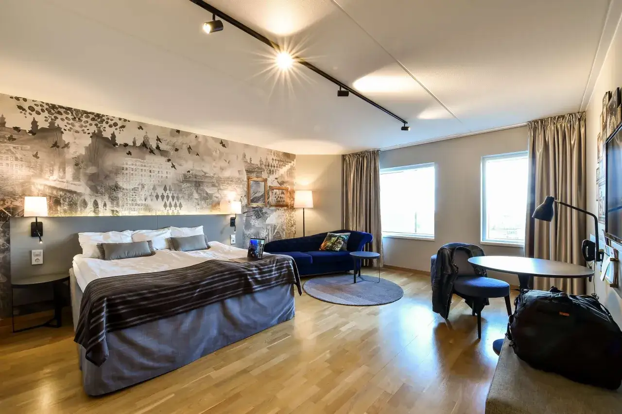 Ett modernt hotellrum med en stor säng, blå soffa och en väggmålning av en stad. Perfekt för dig som söker ett hotell nära Stortorget.