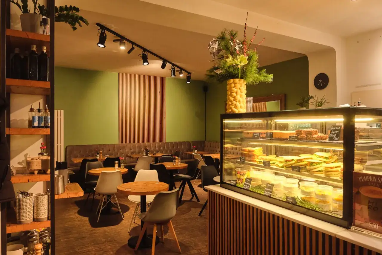 Gem&uuml;tliches Caf&eacute; in Berlin mit gr&uuml;nen W&auml;nden, Holzakzenten und einer Vitrine voller Kuchen und Sandwiches. Perfekt f&uuml;r einen leckeren Smoothie.