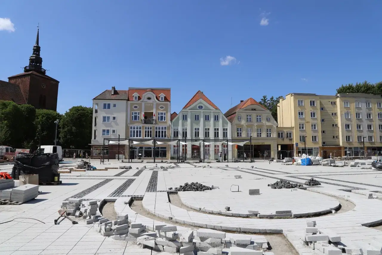 Remontowany stary rynek Słupsk. Widać kościół, kolorowe kamienice i plac budowy z kostką brukową.