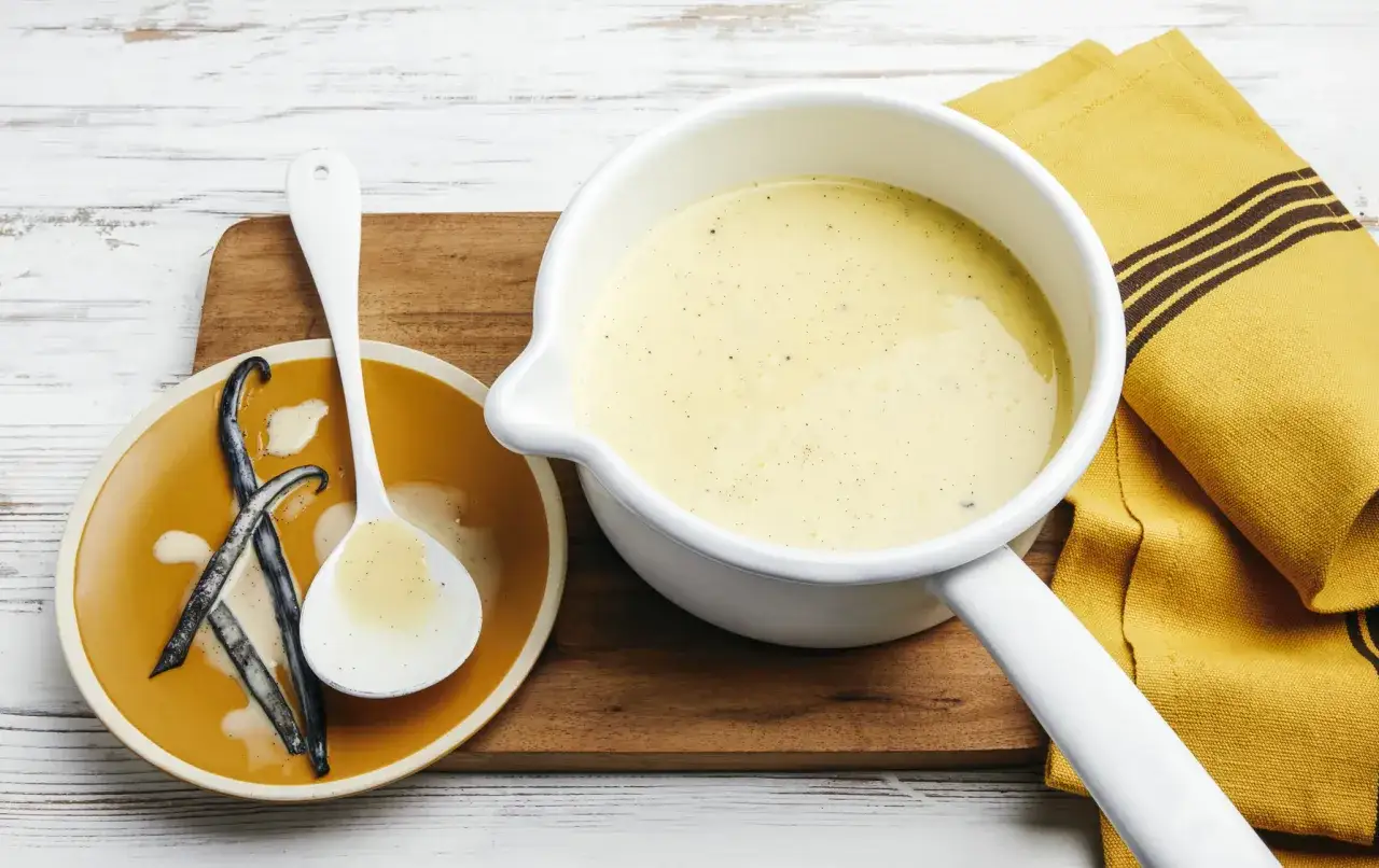 Une casserole de crème anglaise onctueuse, avec des gousses de vanille sur une assiette.