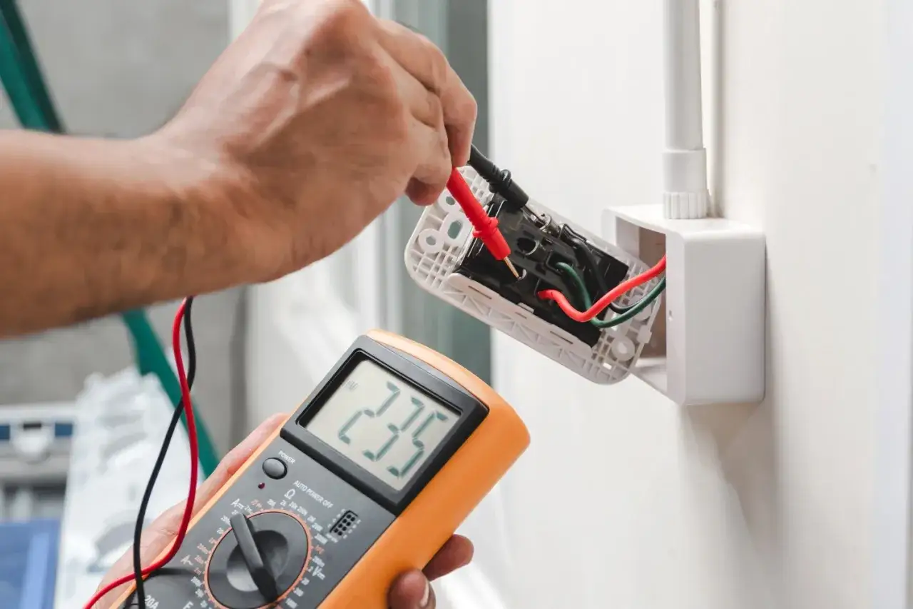 Elektryk sprawdza napięcie multimetrem, szukając problemu z brakiem uziemienia w domu.