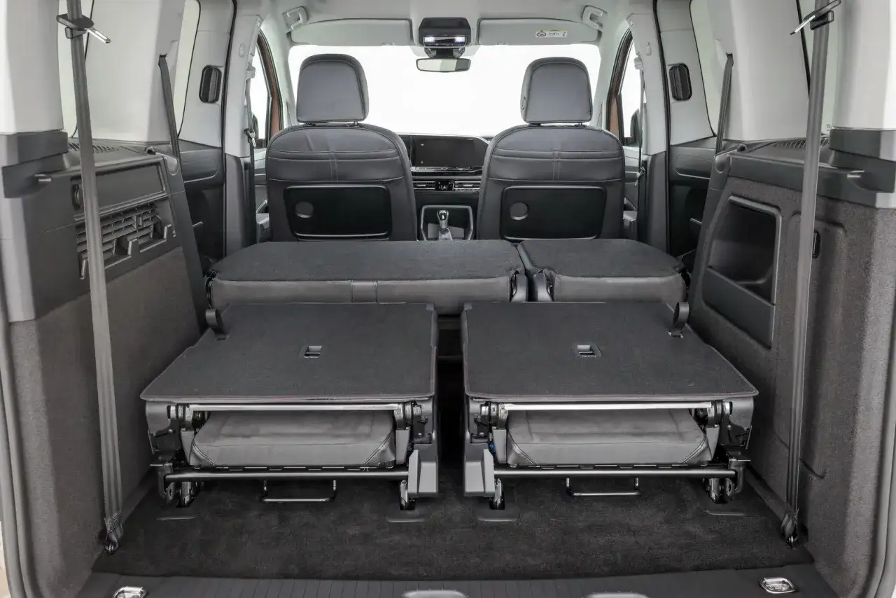 Interni del Volkswagen Caddy con sedili posteriori abbattuti, pronti per caricare bagagli o attrezzature.