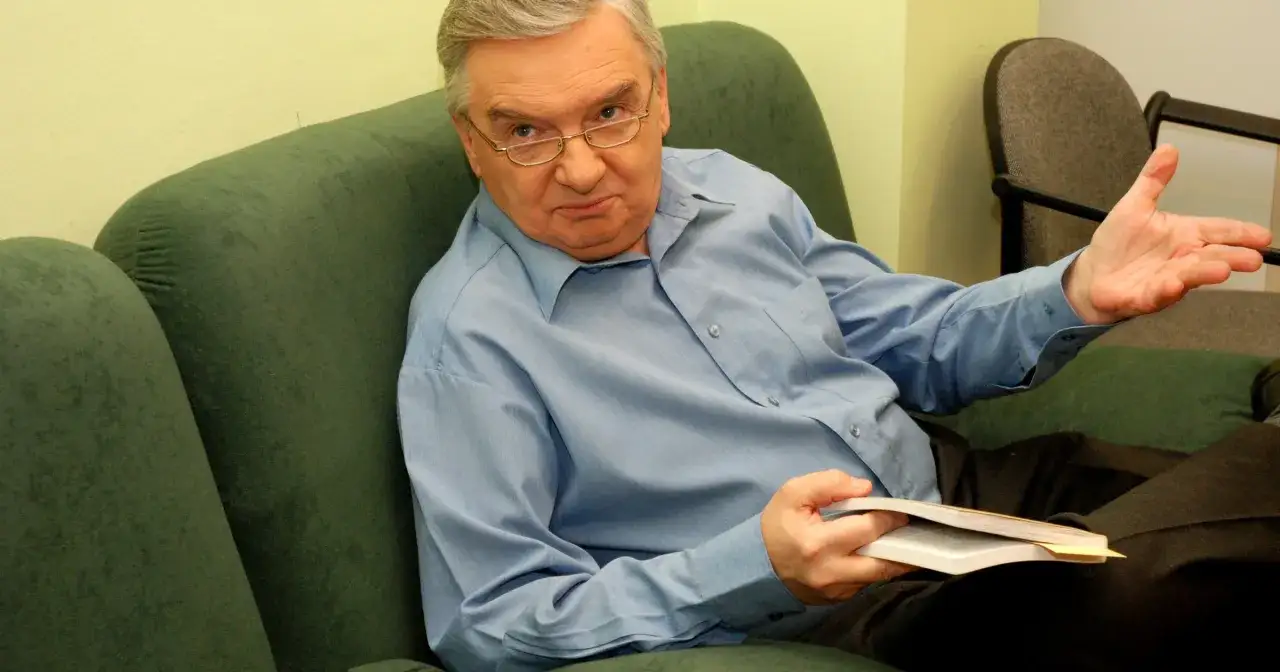 Tadeusz Sznuk, kto prowadzi teleturniej Jeden z Dziesięciu, siedzi na kanapie z książką.