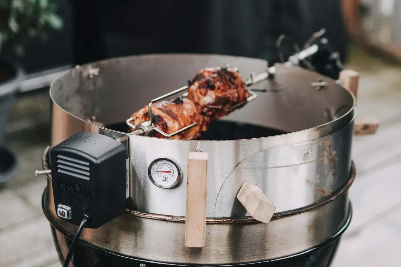 Schweinshaxe sous vide dreht sich am Spieß über glühender Kohle. Ein Thermometer zeigt die Gartemperatur an.
