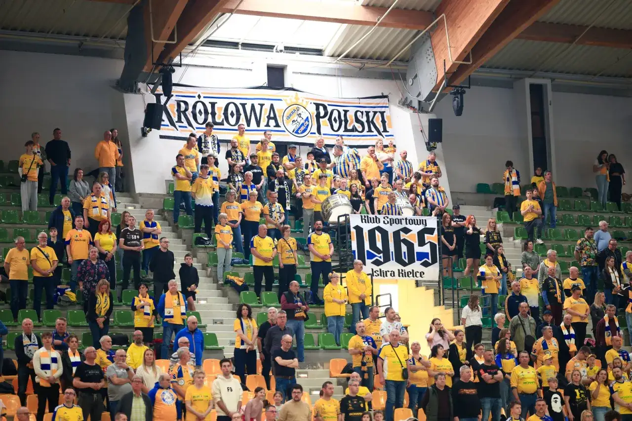 Kibice na meczu Iskra Kielce dopingują swoją drużynę. Wszyscy ubrani w ż&oacute;łto-niebieskie barwy, z transparentem 