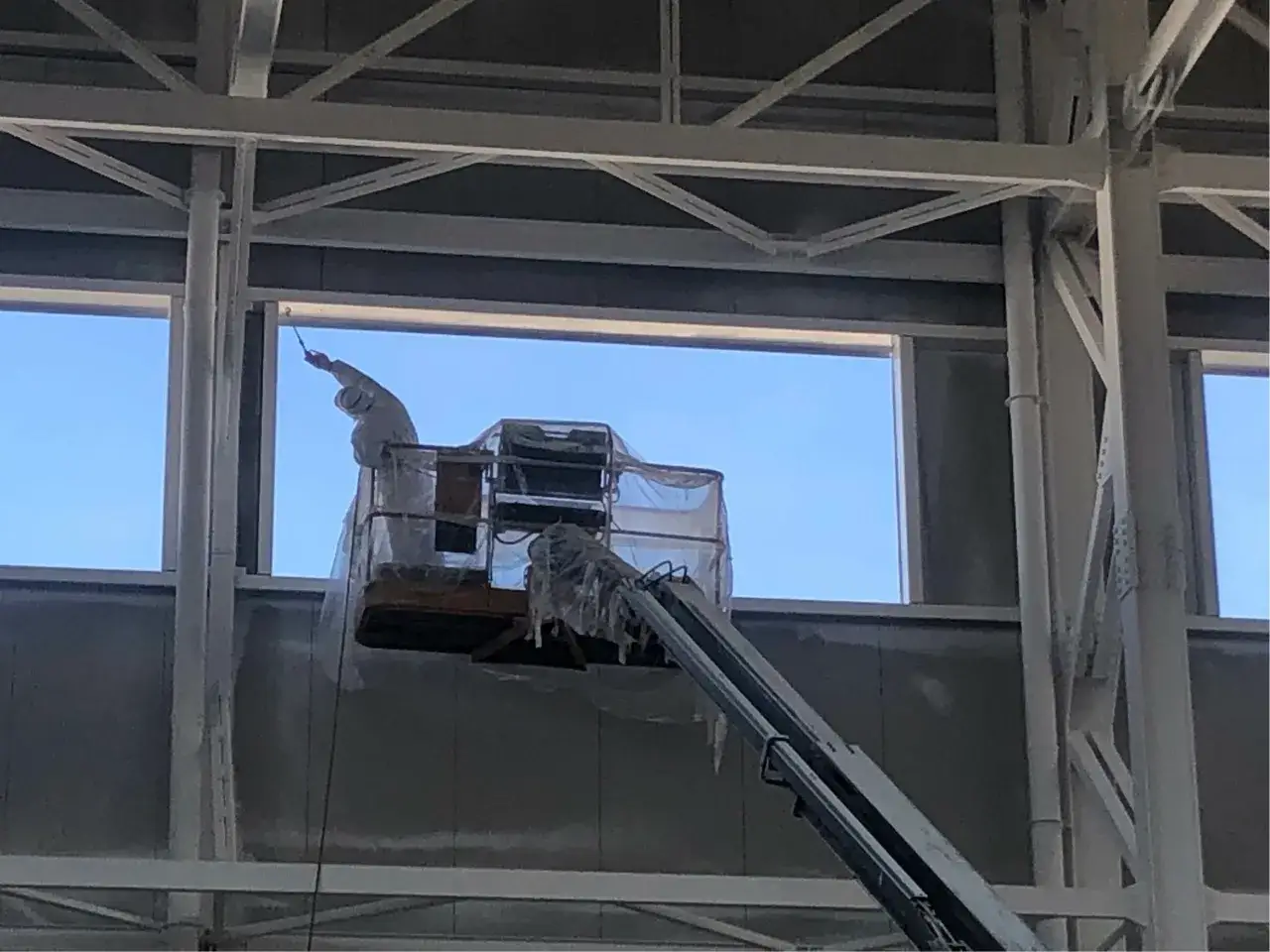 Operaio in cestello elevatore applica pittura ignifuga su travi metalliche di un edificio in costruzione.