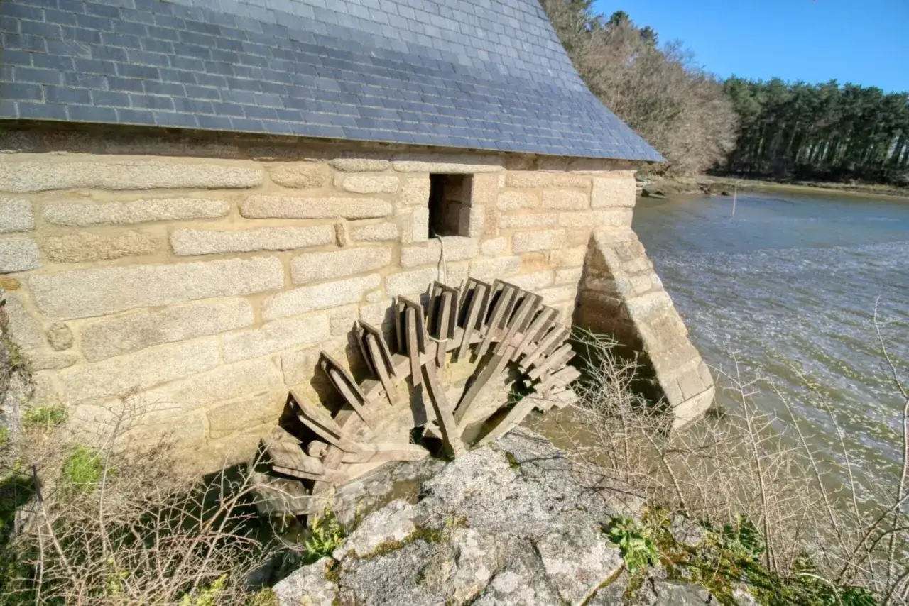 Vieille roue à aubes en bois du Henan, adossée à un moulin en pierre, au bord d'une rivière agitée.
