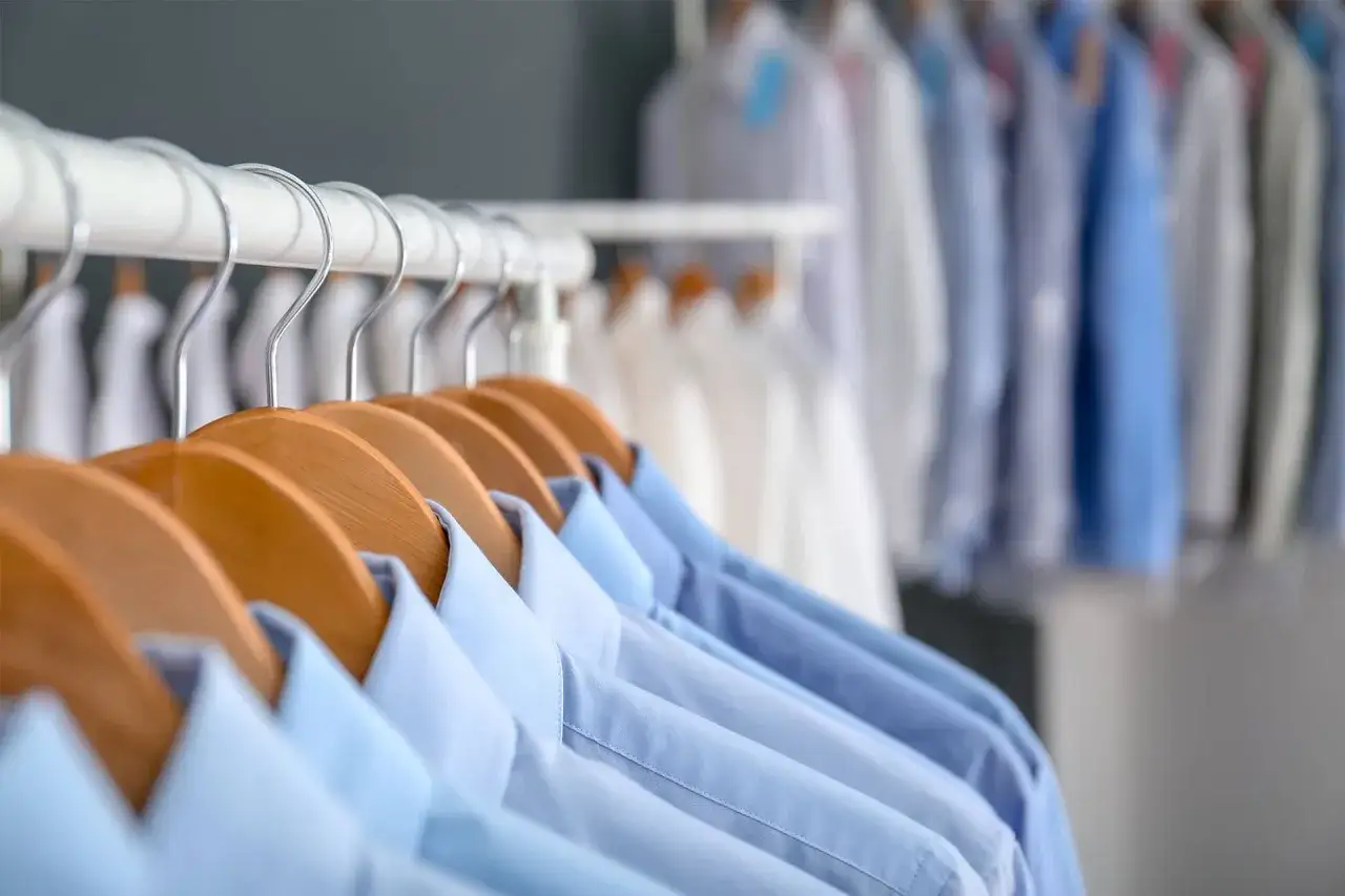Reihe von blauen und wei&szlig;en Hemden auf Kleiderb&uuml;geln, bereit f&uuml;r die chemische Reinigung.