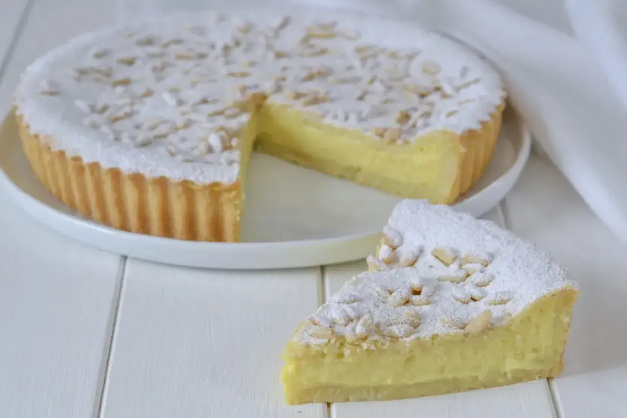 Una fetta di torta della nonna, con crema gialla e pinoli, cosparsa di zucchero a velo.