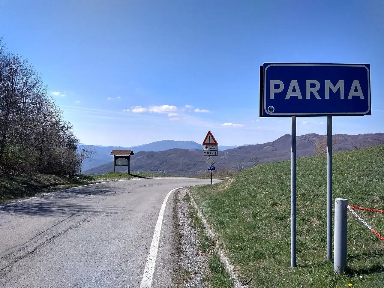 Strada panoramica verso Parma, con cartello stradale e montagne sullo sfondo. Un luogo ideale per una sosta al passo Pellizzone.
