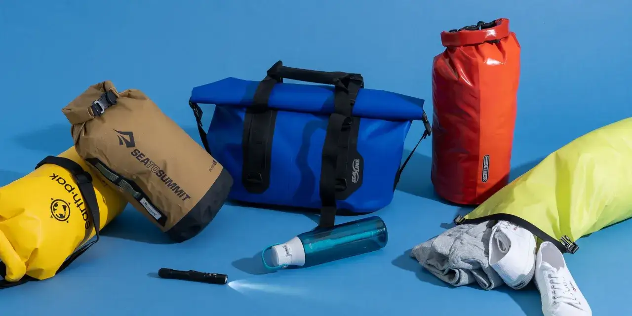 Bolsas de viaje estanco de varios colores, una botella de agua y ropa.