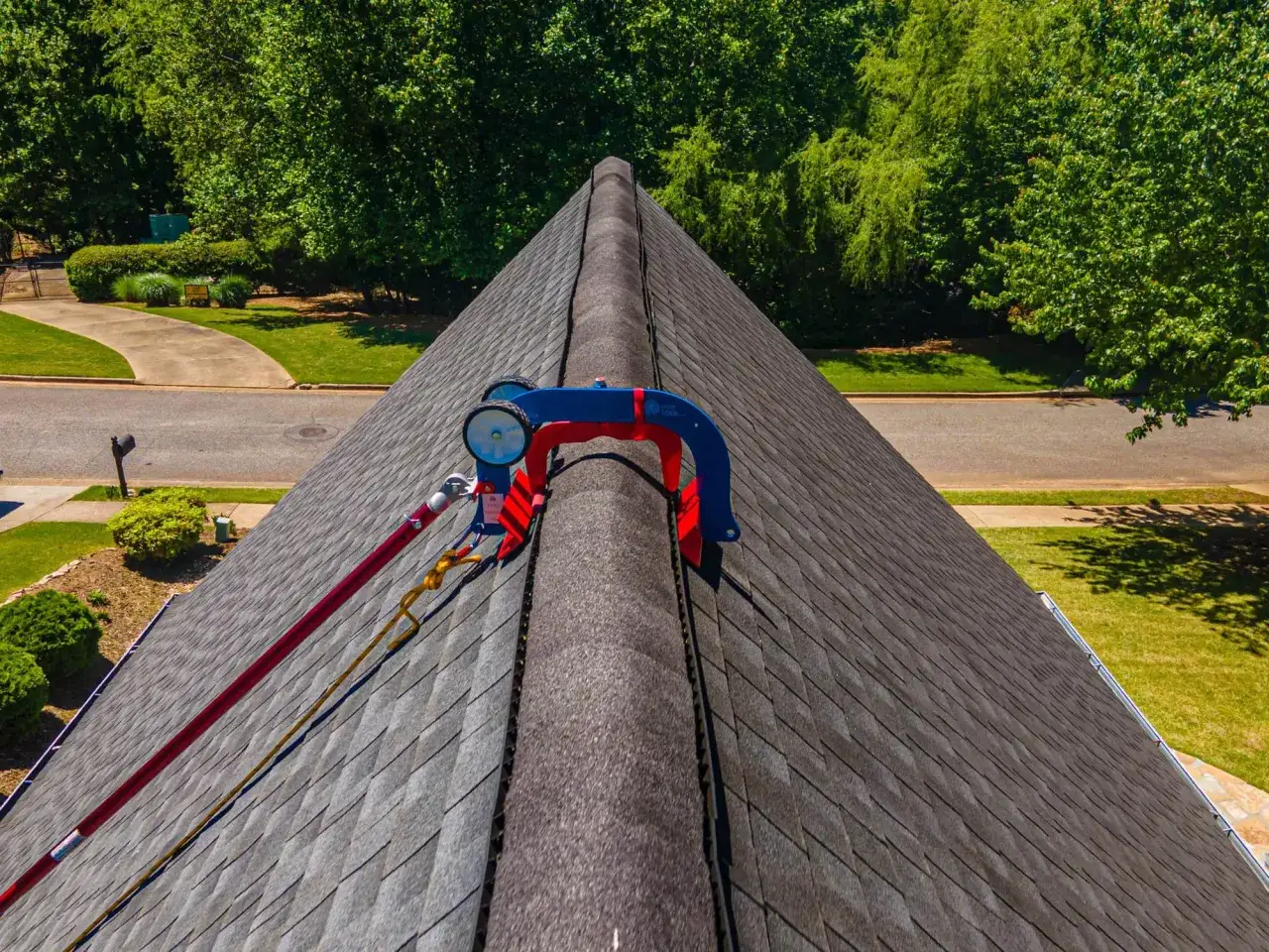 A safety harness and rope system is attached to a ridge vent, demonstrating how to shingle a steep roof safely.
