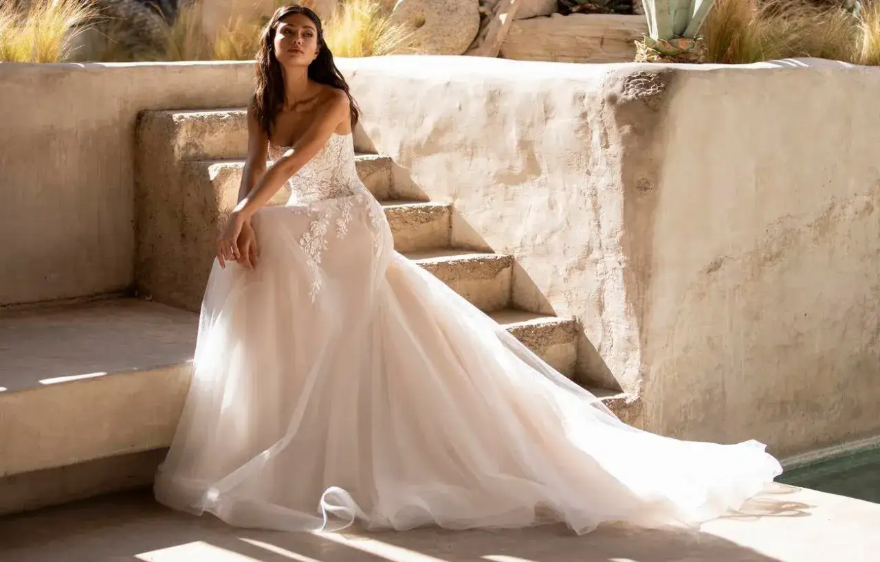Novia con vestido de encaje y tul, lista para su boda mexicana, sentada en escalones de piedra bajo el sol.
