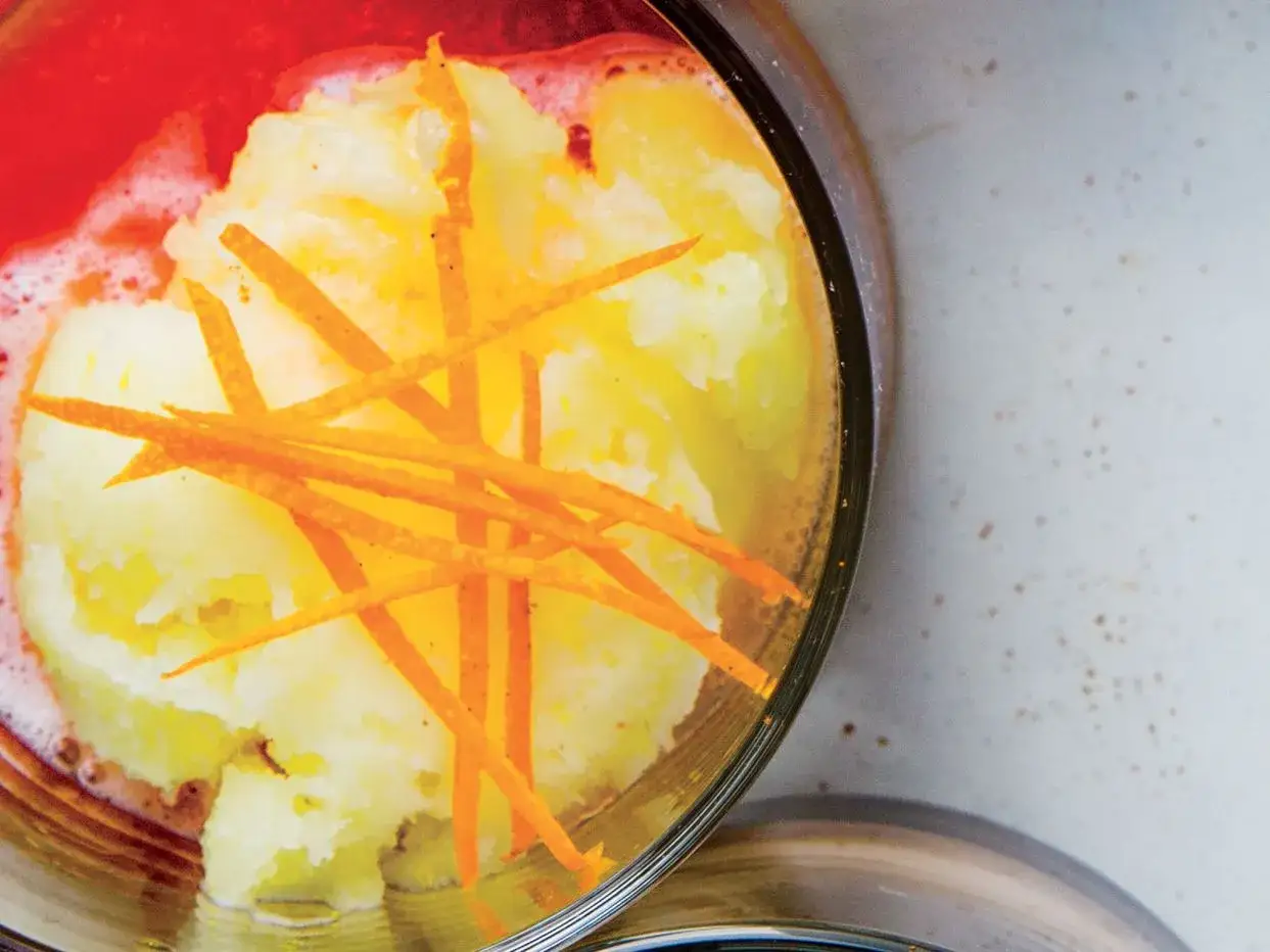 Erfrischendes Campari Sorbet mit Orangenzesten in einem Glas, umgeben von rotem Schaum.