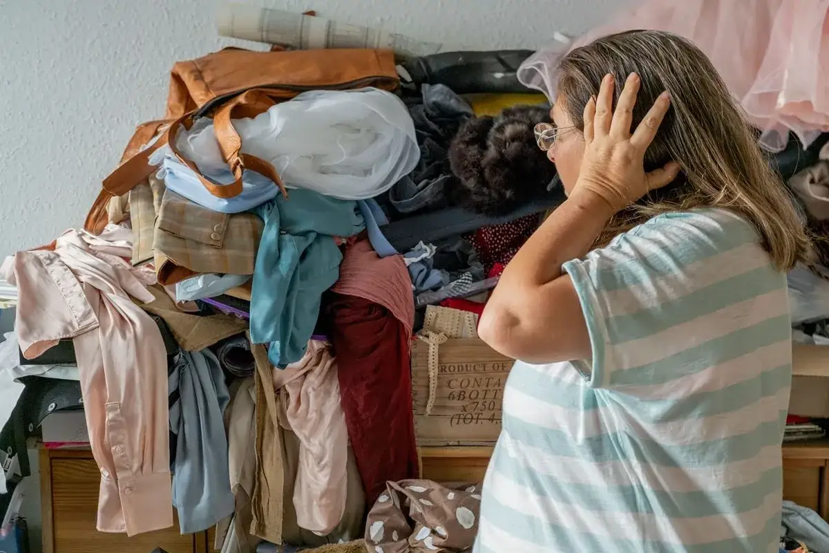 Une femme, accabl&eacute;e par le d&eacute;sordre, semble vouloir **vider sa maison**. Des v&ecirc;tements s'entassent, cr&eacute;ant un chaos visuel.