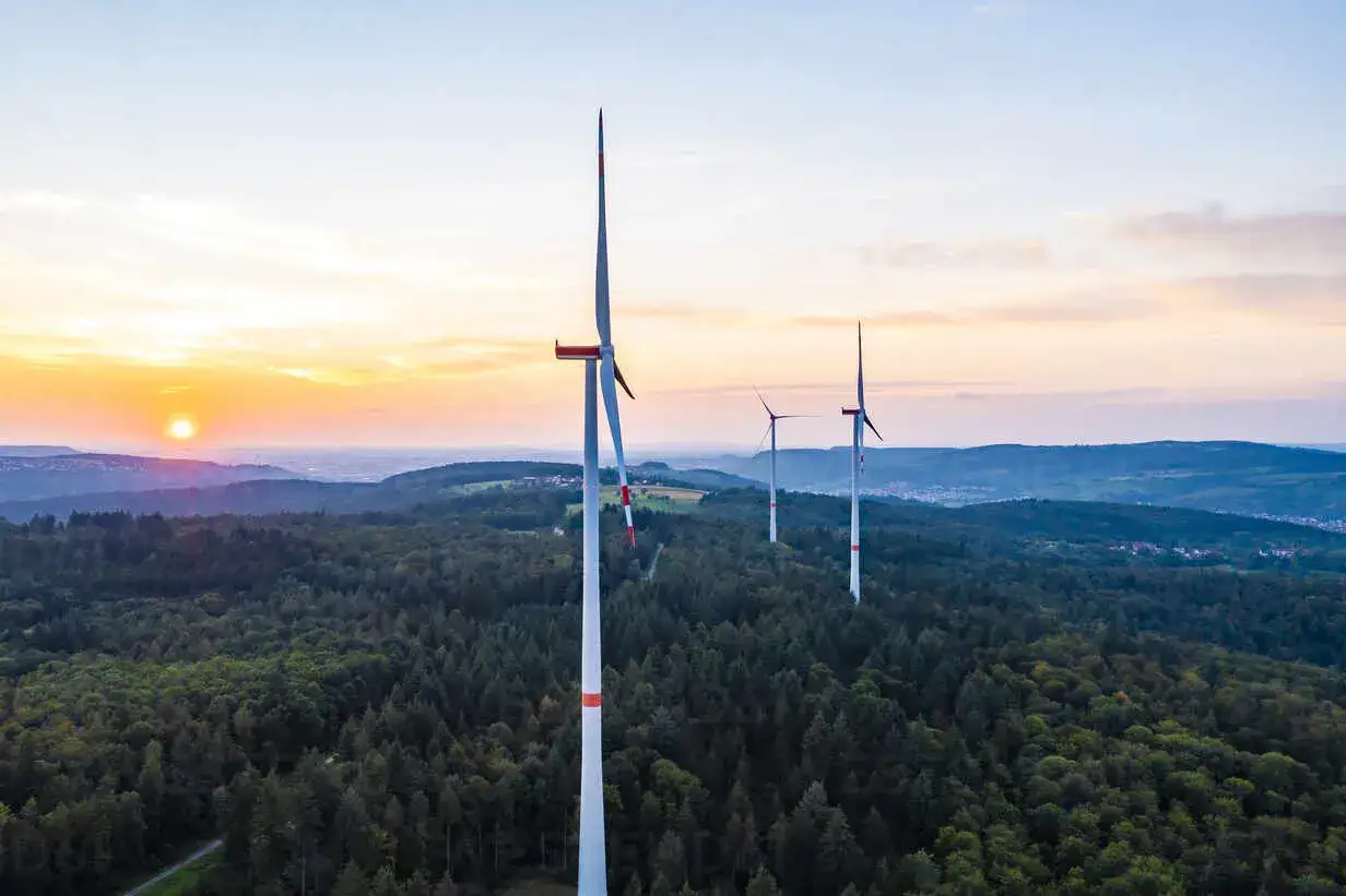 Windräder im Sonnenuntergang über einem Wald in Deutschland. Ein Onshore-Windpark, der saubere Energie erzeugt.