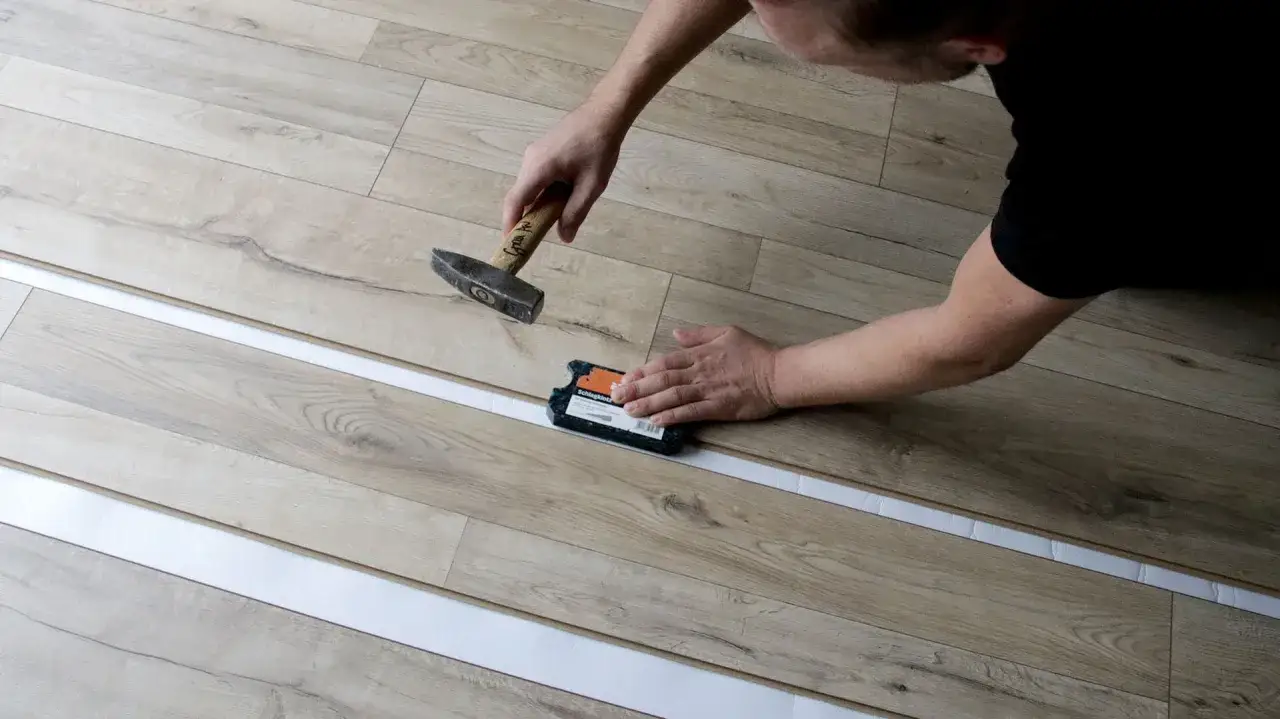 Instalación de tarima flotante: un hombre usa un martillo y un bloque de golpeo para colocar una tabla de suelo laminado.