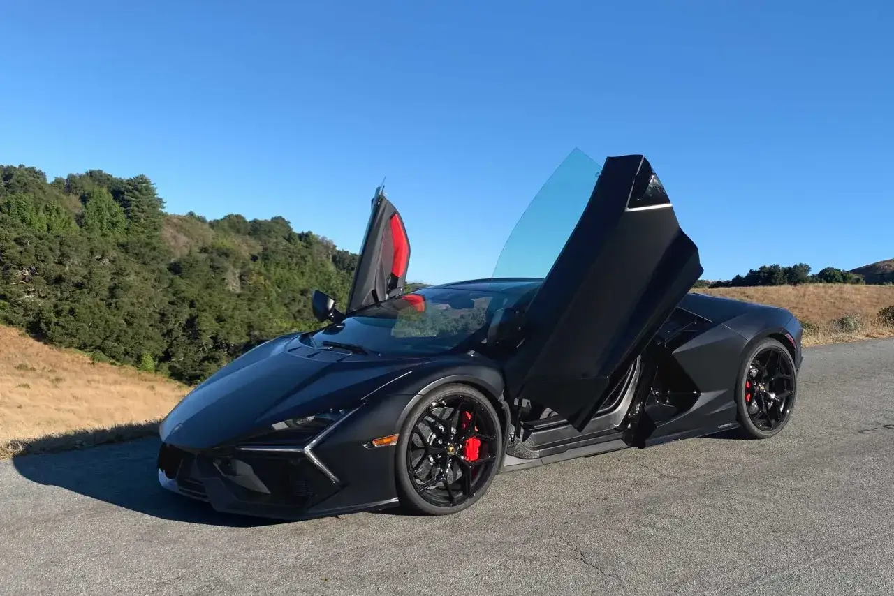 Czarny Lamborghini Revuelto z otwartymi drzwiami, zaparkowany na tle wzgórz i błękitnego nieba.