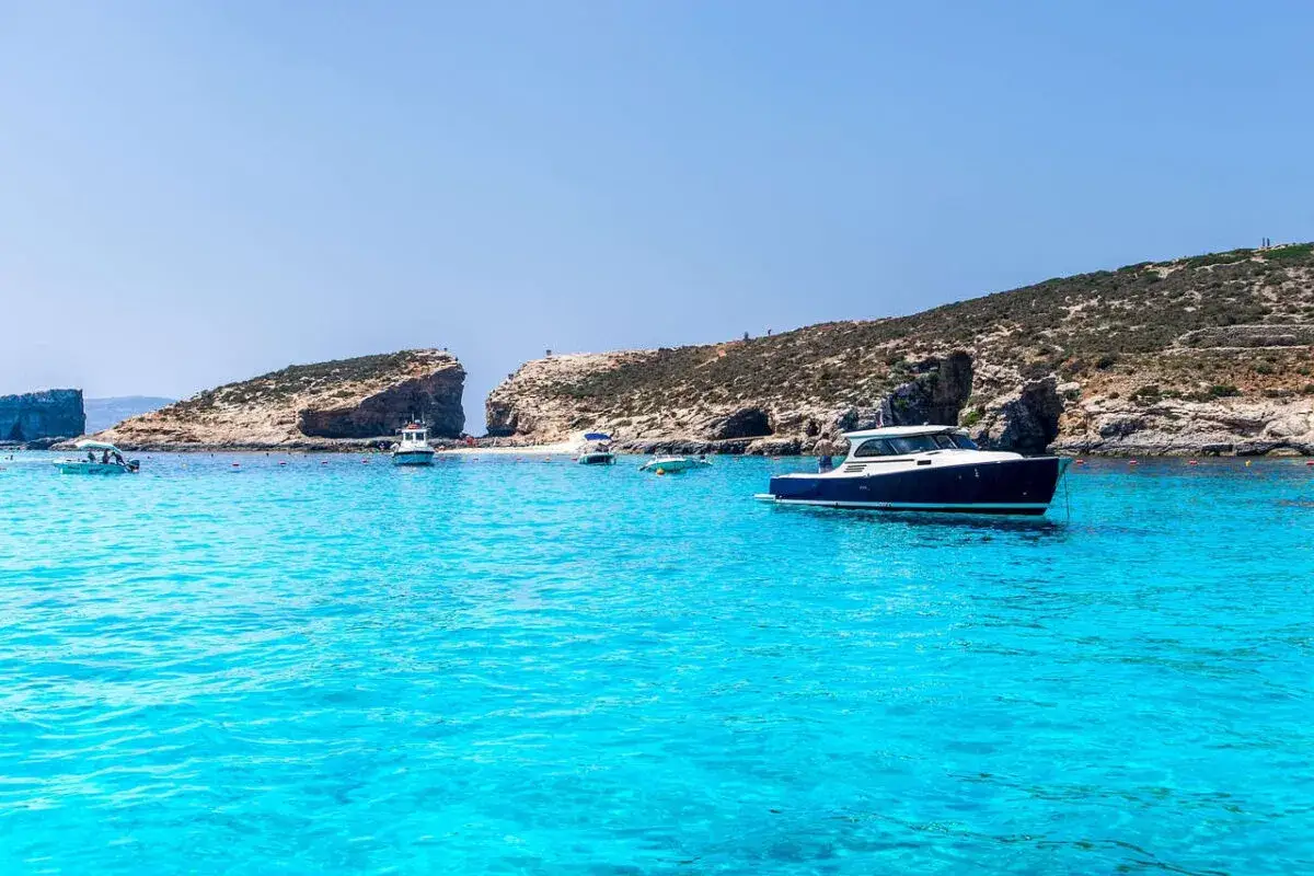 Malta, lipiec: błękitna woda, łodzie i skaliste wybrzeże. Idealna pogoda na wakacje.