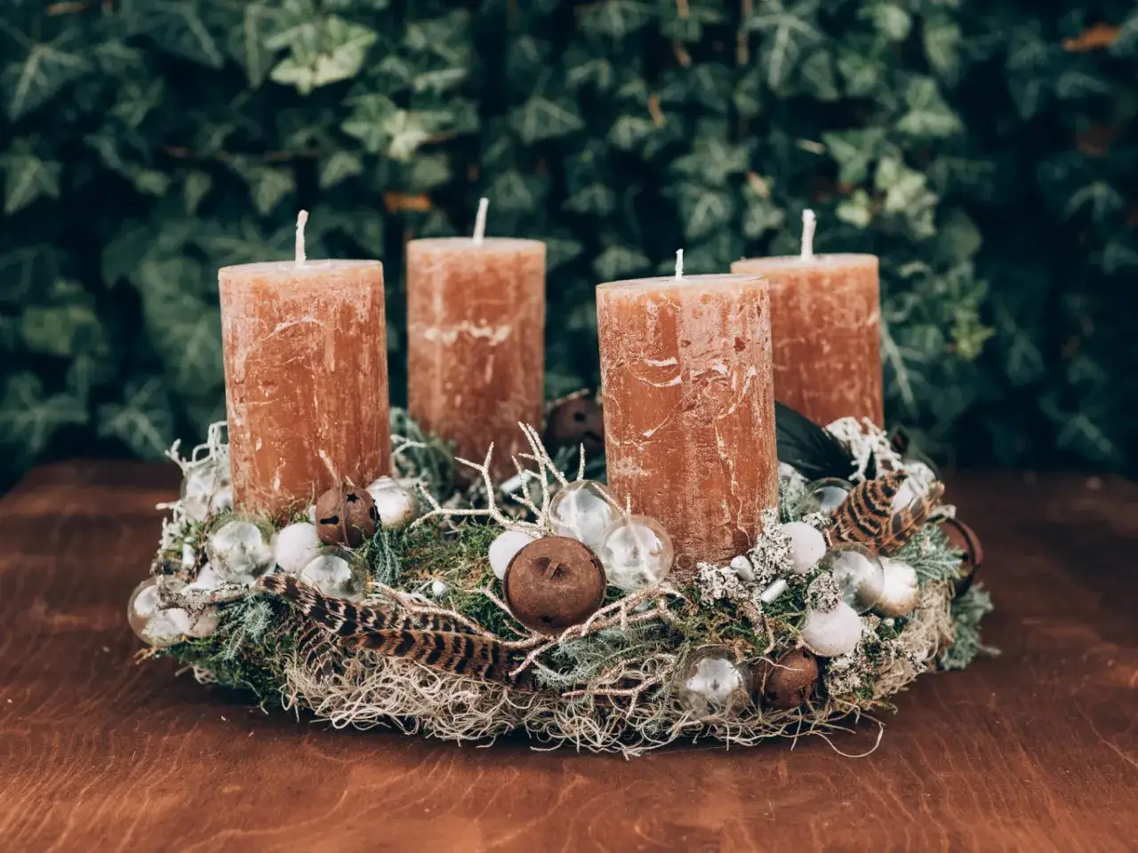 Nat&uuml;rlicher Adventskranz Idee mit vier braunen Kerzen, Moos, Federn und kleinen Glaskugeln.