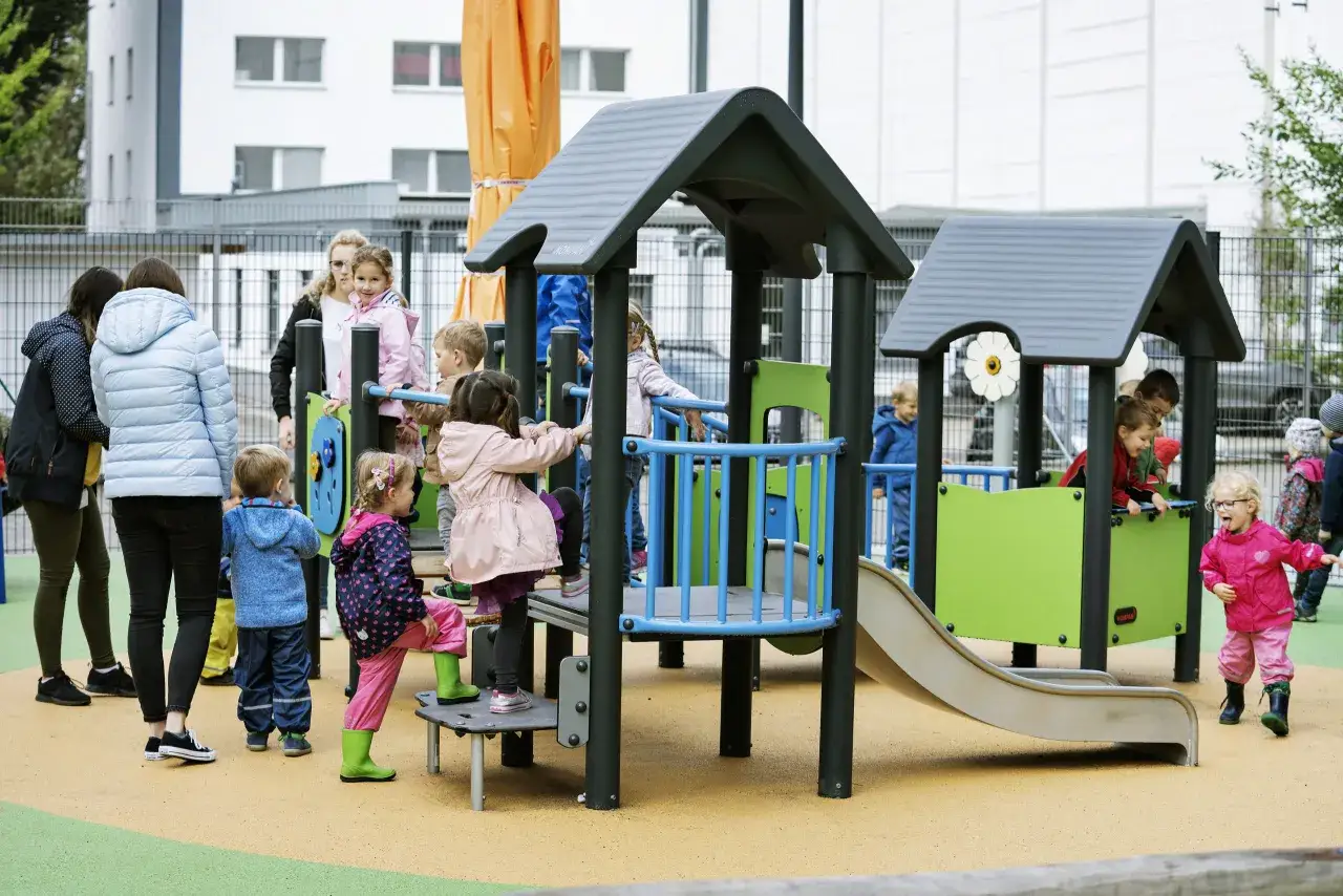 Dzieci bawią się na placu zabaw, jedno dziecko dotyka inne dzieci, śmiejąc się i biegając.