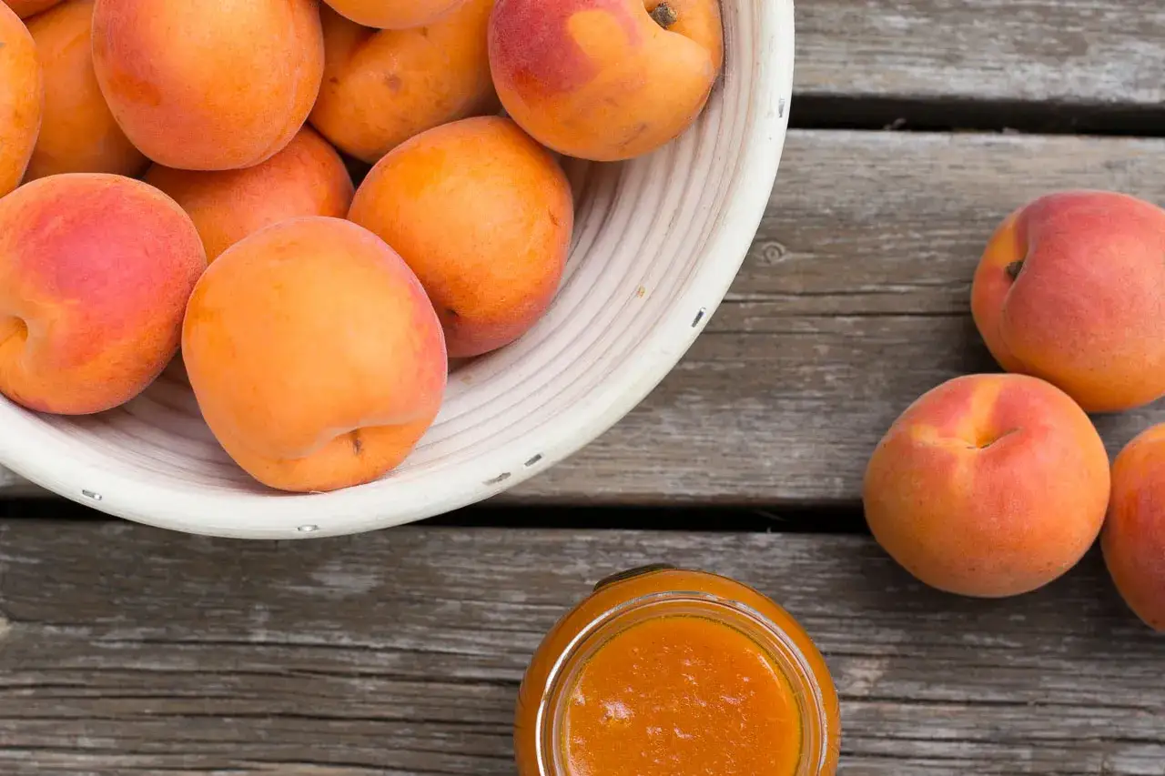 Frische Marillen und Aprikosen liegen neben einem Glas Marmelade. Der Unterschied zwischen Marille und Aprikose ist oft nur eine Frage der Region.
