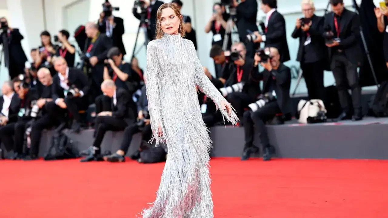 Isabelle Huppert, éblouissante dans sa robe argentée à franges, foule le tapis rouge de la Mostra de Venise, sous le regard des photographes.