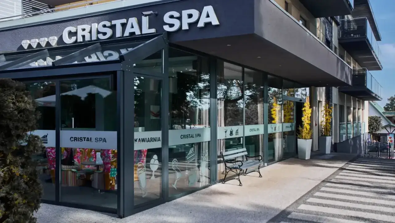 Elegancki budynek hotelu Cristal Spa z przeszklonym wejściem i kawiarnią. Na fasadzie widoczny napis 