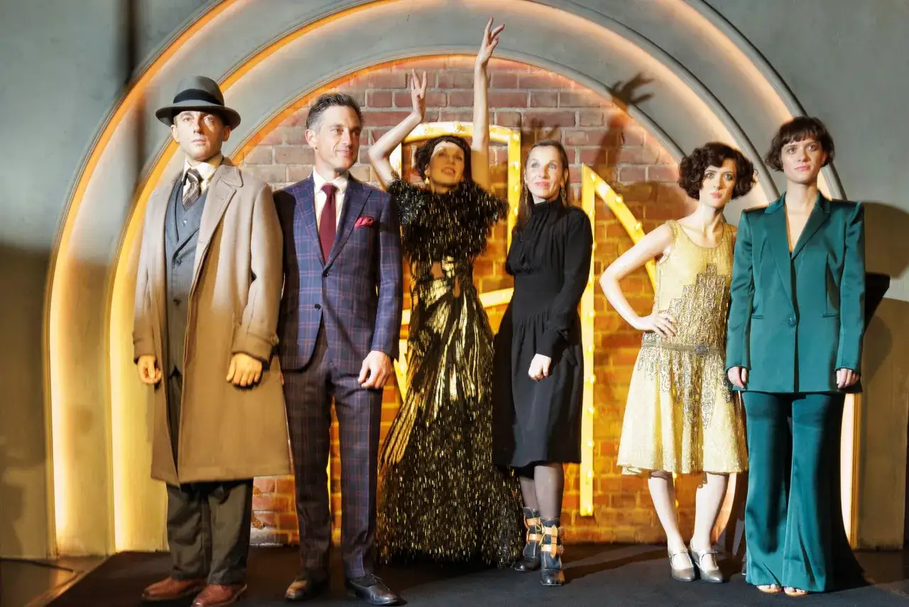 Ensemble von Babylon Berlin Staffel 5: Ein Mann im Trenchcoat, ein Mann im Anzug, eine Frau im goldenen Kleid, eine Frau im schwarzen Kleid und zwei Frauen in Hosenanz&uuml;gen.