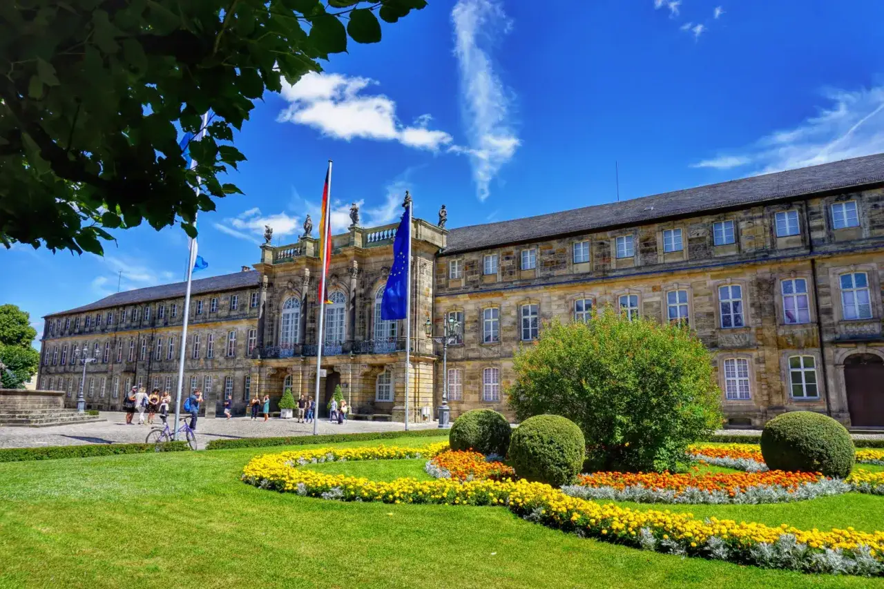 Markgrafen Bayreuth: Prachtvolles Neues Schloss mit blühendem Garten und Fahnen im Sonnenschein.