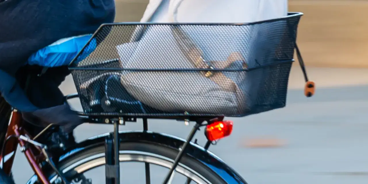 Anleitung: Fahrradkorb hinten befestigen. Ein schwarzer Drahtkorb mit Gepäck ist auf einem Fahrrad montiert.