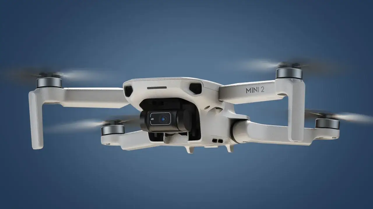 Eine DJI Mini 2 Drohne mit 4K-Kamera schwebt vor blauem Himmel. Die Propeller drehen sich, bereit für Aufnahmen mit der DJI Mini 2 App.