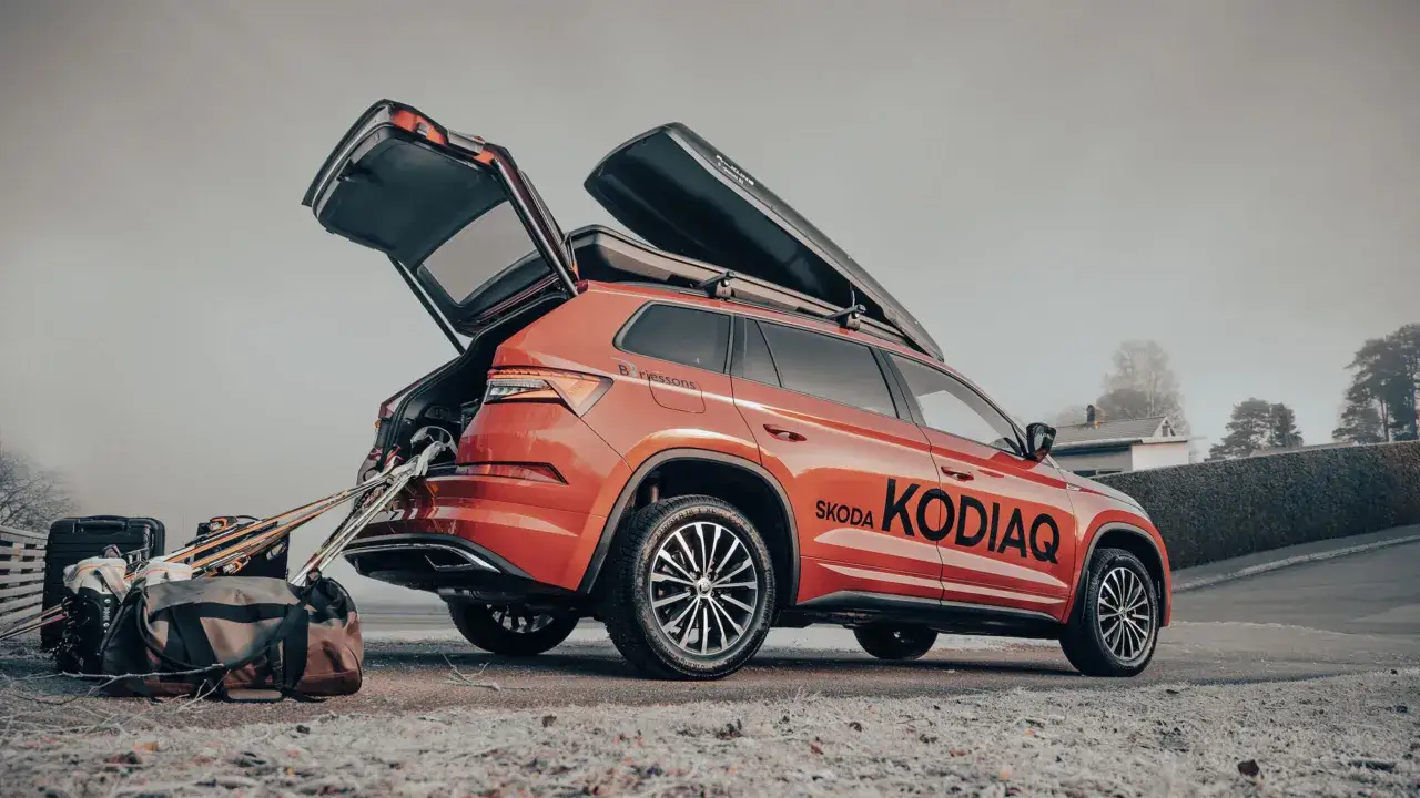 Röd Skoda Kodiaq redo för vinterns äventyr med takboxar och packning. Skidutrustning och väskor står redo vid den öppna bakluckan.