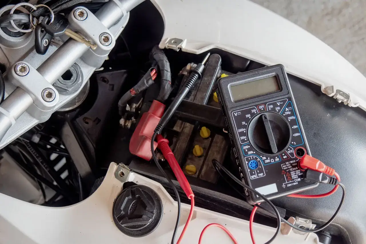 Multimetro collegato alla batteria di un motorino per diagnosticare problemi motorino avviamento. Chiavi del veicolo in primo piano.