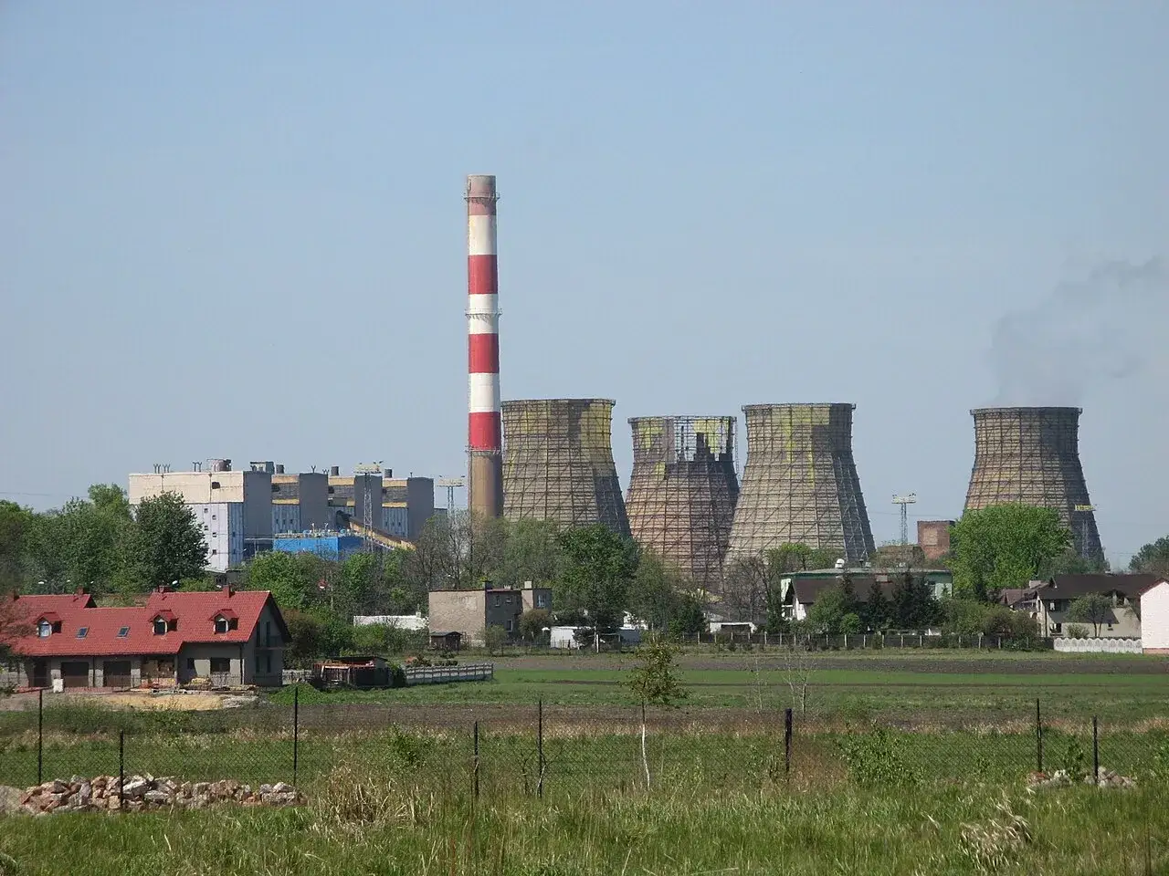 Industrielle Anlage in Polen mit Kühltürmen und einem roten-weißen Schornstein, die Strom erzeugt.