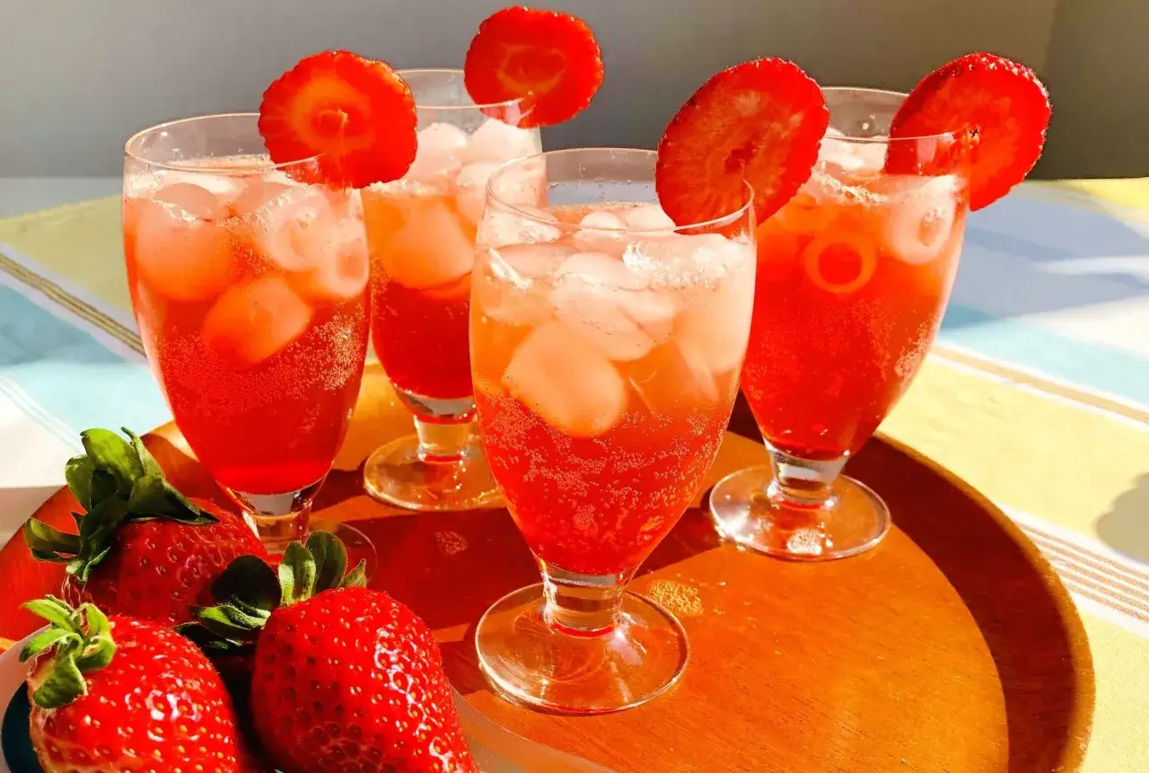 Fyra glas med tinto de verano, is och jordgubbskivor, på ett träfat med färska jordgubbar.