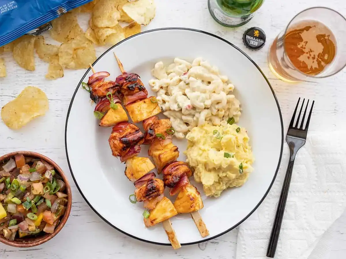 Brochettes de poulet grill&eacute; avec ananas et oignons rouges, accompagn&eacute;es de salade de macaronis et de pur&eacute;e de pommes de terre. Un repas parfait pour un barbecue.