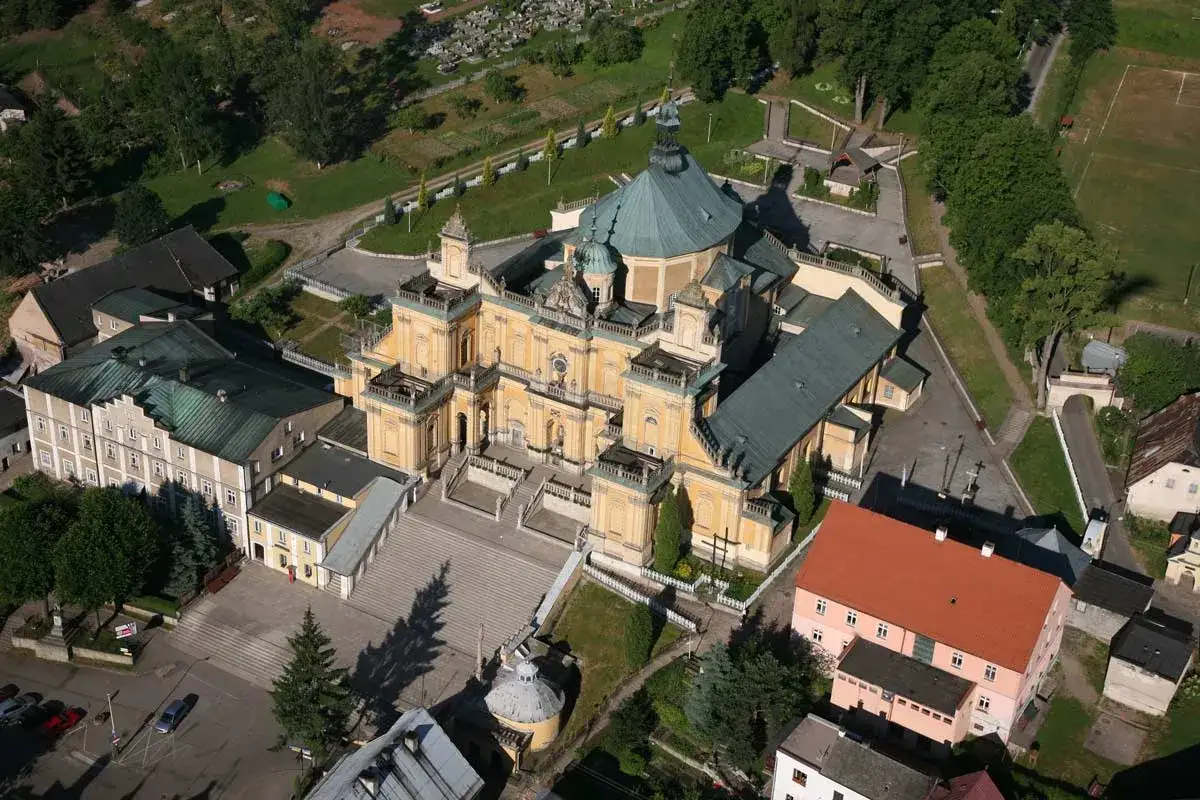Imponująca bazylika Nawiedzenia NMP w Wambierzycach z lotu ptaka, otoczona zielenią i innymi budynkami.