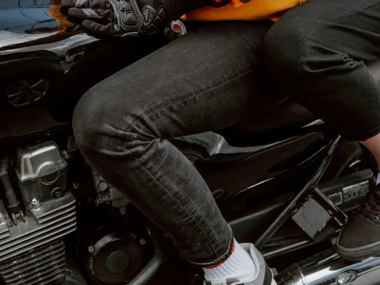 Person sitzt auf einem Motorrad, tr&auml;gt schwarze Hose, Handschuhe und Sneakers. Die schwarze Hose ist bereit zum Waschen.