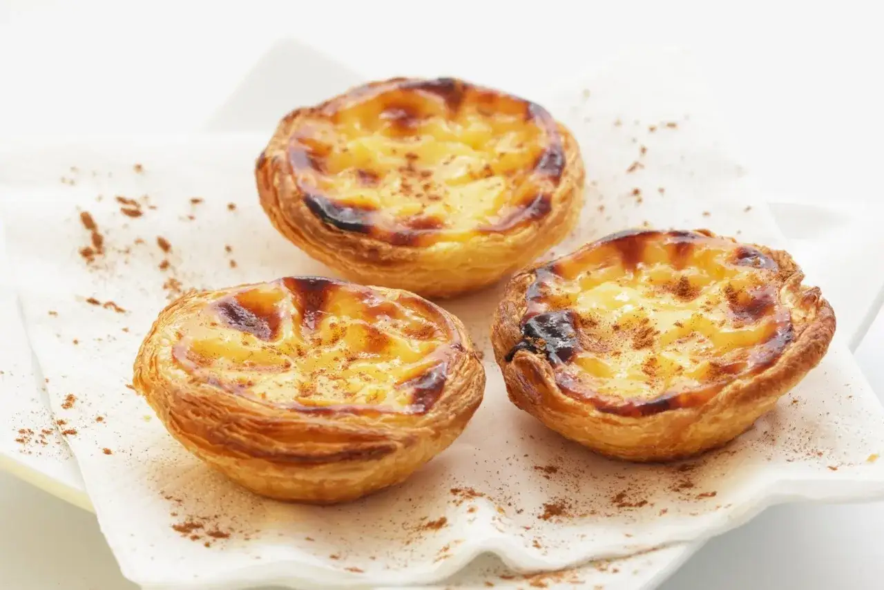 Tre deliziosi pastéis de nata, un must per sapere cosa mangiare a Lisbona, cosparsi di cannella su un tovagliolo bianco.