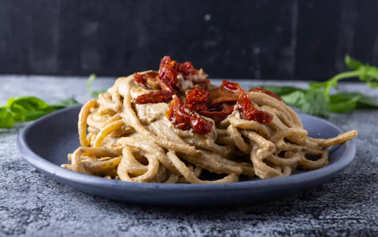 Un piatto di pasta cremosa con pomodori secchi, guarnito con basilico fresco.