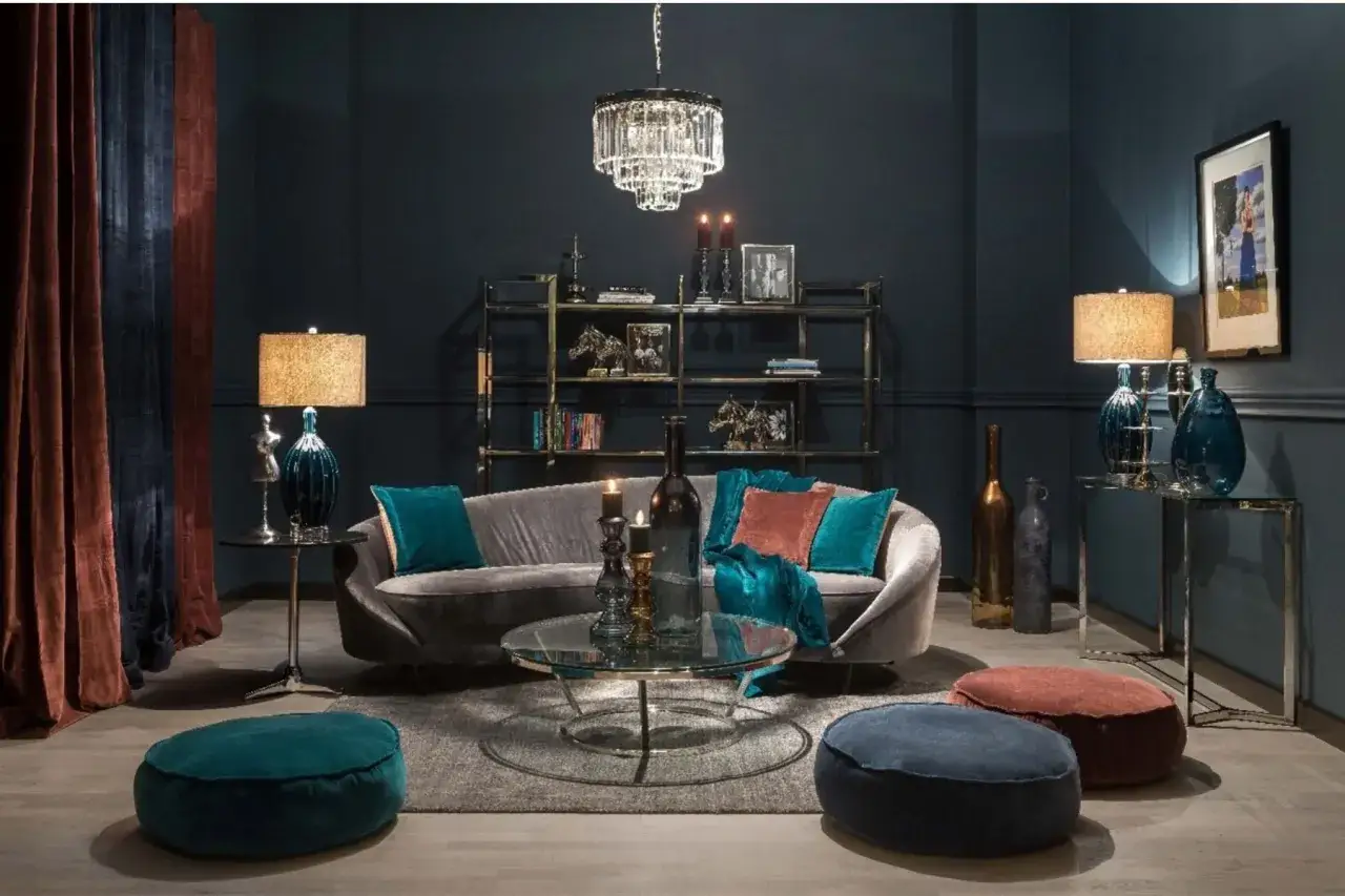 Elegancki salon z sofą w kolorze navy, turkusowymi i rudymi poduszkami, szklanym stolikiem i kryształowym żyrandolem.