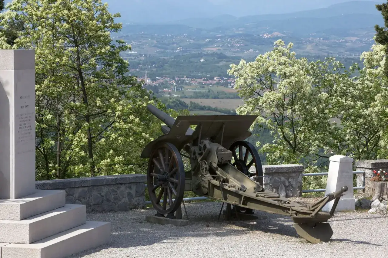 Cannone d'epoca su un colle fiorito, con un monumento alla memoria. Un luogo che ricorda come la morte si sconta vivendo, con la speranza che la pace prevalga.
