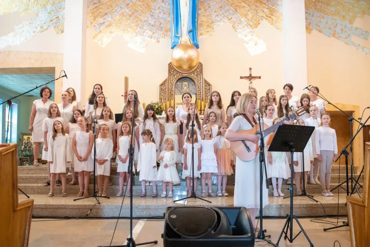 Chór dziecięcy w białych strojach śpiewa w kościele. Kobieta gra na gitarze. Oto jest dzień pełen muzyki.